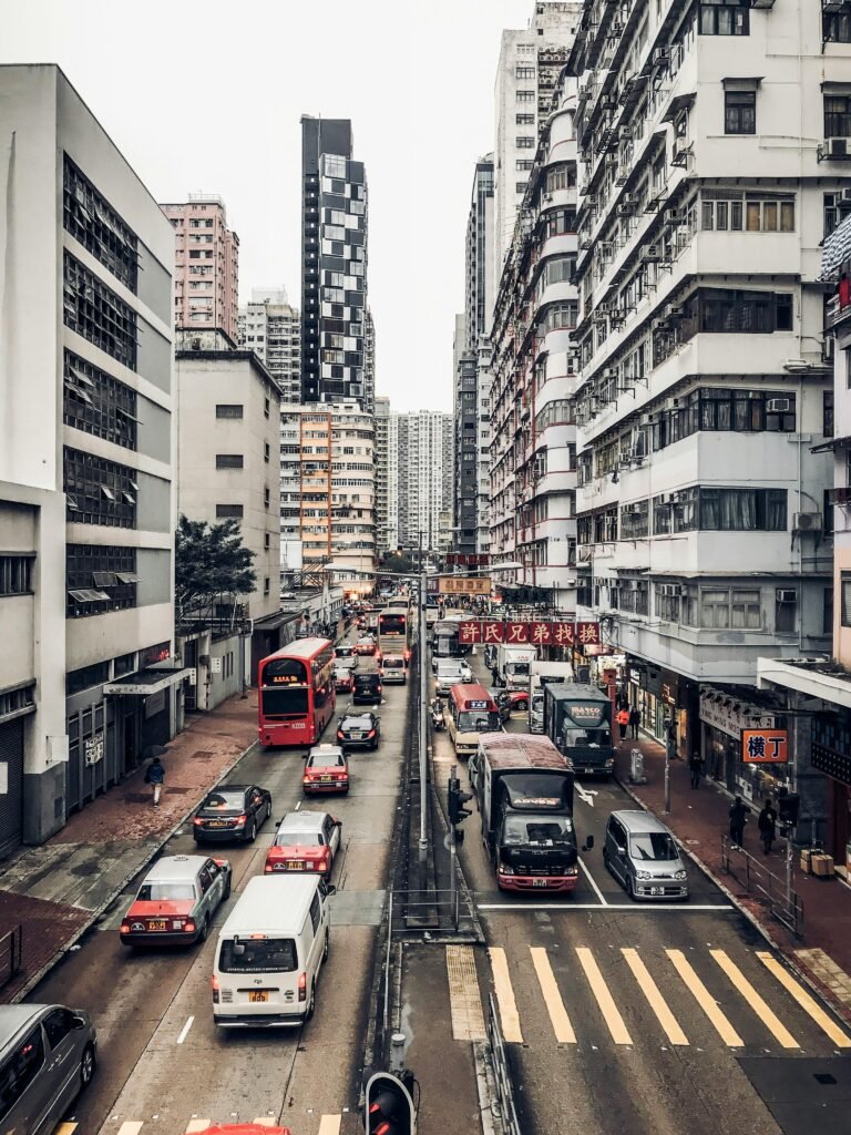 "Busy street in Hong Kong with tall residential buildings on both sides, filled with cars and pedestrians, showing urban city life."